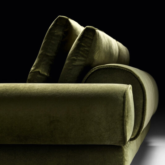 Contemporary Retro Inspired Designer Sofa Close-up of a luxurious Contemporary Retro Inspired Designer Sofa set against a black background. The image highlights the sofa's plush cushions and sleek, modern design with clean lines and smooth fabric texture. The lighting accentuates the richness and depth of the green color, offering a contemporary retro-inspired charm.