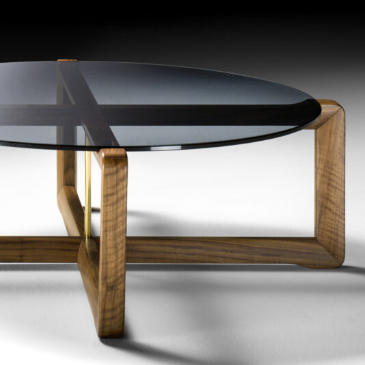 Contemporary Walnut Round Glass Coffee Table The Contemporary Walnut Round Glass Coffee Table features a round glass top supported by a geometric wooden frame. The walnut legs intersect in an X shape beneath the glass surface, showcasing smooth curves and clean lines for a sleek, modern look.