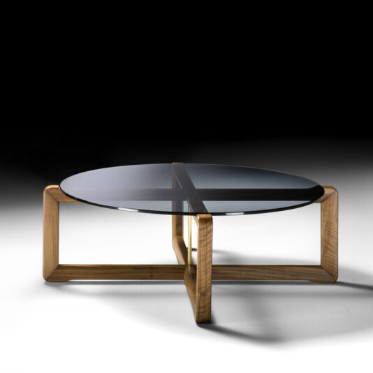 The Contemporary Walnut Round Glass Coffee Table, featuring a wooden base with an intersecting design that forms four quadrants beneath its glass top, is set against a dark gradient background.