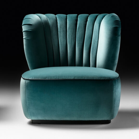 A luxurious Designer Upholstered Velvet Occasional Chair in a plush teal hue, featuring a distinctive scalloped backrest. The chair is showcased against a gradient black to grey background, highlighting its elegance and sophistication.