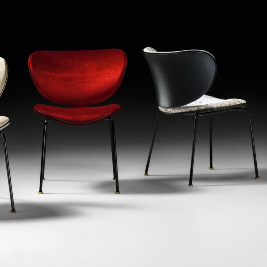 A photograph displays a set of High End Designer Retro Style Dining Chairs, showcasing three sleek and stylish designs. The leftmost chair has a beige seat, the middle one is adorned with a vibrant red seat, and the rightmost chair features a black back paired with a white patterned seat. Each dining chair in the set has thin black legs.
