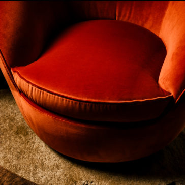 Luxury Designer Velvet Swivel Armchair Close-up of the Luxury Designer Velvet Swivel Armchair, featuring a plush, round design in a vivid red-orange velvet with a thick cushioned seat, resting on a muted light brown carpeted floor. The chair's vibrant fabric stands out against the soft, neutral-colored surroundings.