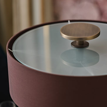 Modern Marble Designer Bronze Table Lamp A close-up of the Modern Marble Designer Bronze Table Lamp, featuring a cylindrical burgundy fabric shade, a circular frosted glass surface on top, and a central round bronze-colored knob. The lamp emits a soft light that accentuates its sleek and sophisticated design against its polished marble base.
