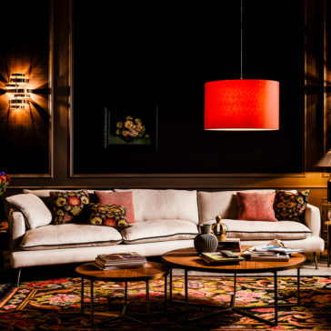 Contemporary Designer Modular Linen Sofa A cozy living room featuring the Contemporary Designer Modular Linen Sofa adorned with colorful patterned pillows, a vibrant red pendant lamp overhead, and two wooden coffee tables topped with decorative items. The dark walls showcase framed artwork, while a patterned rug adds warmth to the space.