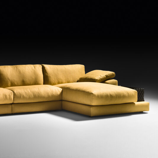 Exclusive Linen Modular Chaise Style Corner Sofa An Exclusive Linen Modular Chaise Style Corner Sofa in a contemporary L-shaped design and vibrant yellow color is set against a stark black background. The overstuffed cushions look exceptionally soft, and a woven basket can be seen partially behind the chaise section.