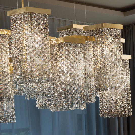 Italian Smoky Crystal Brass Contemporary Chandelier The Italian Smoky Crystal Brass Contemporary Chandelier graces the ceiling with its luxurious, contemporary design. Multiple rectangular, cascading tiers of smoky crystals and brass accents complement the draped curtains, creating an elegant and opulent ambiance in the room.