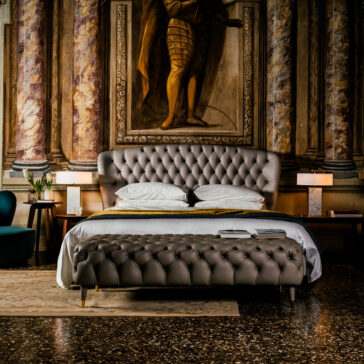 A lavish bedroom features a Designer Leather Button Upholstered Luxury Bed with bench, an opulent mural with a historical figure, elegant lamps, a green armchair, and a rug on the dark patterned floor, creating a sophisticated ambiance.