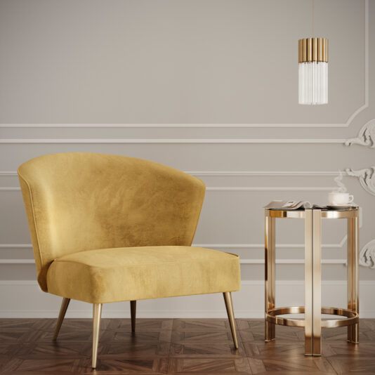 A modern interior showcasing a mustard yellow armchair with sleek lines, positioned on a wooden floor. Next to it is the Art Deco Inspired Designer Contemporary Luxury Side Table with a glass top, holding a white teacup and saucer. A pendant light with a cylindrical glass shade hangs from the ceiling.