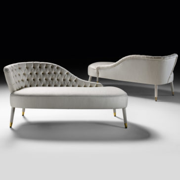 Two Button Upholstered Designer Linen Chaise Longues, featuring curved backrests and smooth linen upholstery in a light color, are set against a black background. The chaise longues showcase sleek, tapered legs with gold-toned accents at the feet.