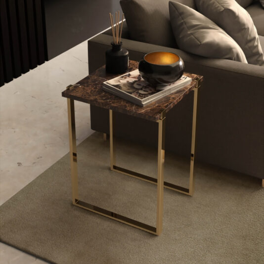 Designer Art Deco Inspired Luxury Side Table Nest A modern living room features a gray couch with multiple cushions on a soft beige rug. Beside the couch is the Designer Art Deco Inspired Luxury Side Table Nest, showcasing a marble top and gold legs. Atop this stylish piece sits a small black vase with reeds, a stack of books, and a decorative bowl.