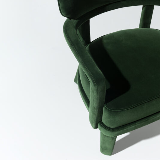 Contemporary Small Velvet Armchair A Contemporary Small Velvet Armchair is partially visible against a plain white background. The green chair, featuring a curved backrest and smooth, plush upholstery, boasts an elegant minimalist design that exudes both luxury and modernity.