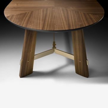 The Contemporary Designer Oval Walnut Dining Table features a polished dark walnut surface and stands on three wide, angled legs supported by metallic connectors. It is stylishly showcased on a simple, light-colored floor with a gradient gray background.