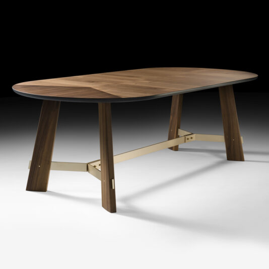 A Contemporary Designer Oval Walnut Dining Table with a polished top featuring rounded edges. The table stands on four sturdy legs connected by a horizontal metal support bar. The background is a gradient transitioning from white at the bottom to black at the top.