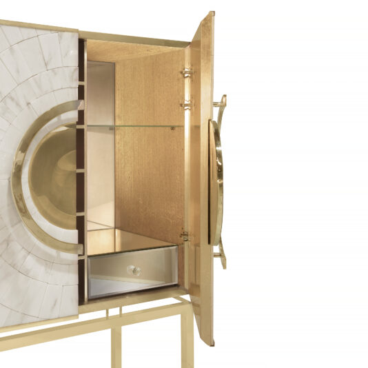 Exclusive Marble Art Deco Inspired Contemporary Cabinet The Exclusive Marble Art Deco Inspired Contemporary Cabinet is a trendy piece featuring a contemporary, gold-colored exterior with white and gold geometric patterns. One door is partially open, revealing a glass shelf and a small drawer inside. The cabinet stands on four slim, gold legs for a stylish look.