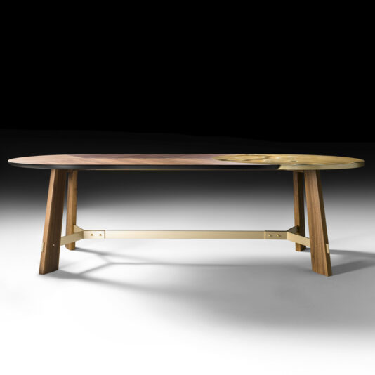 The Oval Walnut And Marble Contemporary Designer Dining Table features an oval-shaped top combining natural walnut and marble sections. This modern wooden dining table stands on four angular legs connected by a horizontal support beam, ensuring stability. The dark background accentuates the table's sleek design.