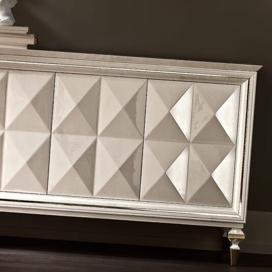 A close-up of the Italian Diamond Design Mother of Pearl Sideboard showcases its elegant front panels adorned with a geometric, pyramid-patterned design. The piece features a glossy finish and delicate, angled legs, standing against a dark, solid-colored wall. Its mother of pearl accents add a touch of opulence to the overall aesthetic.