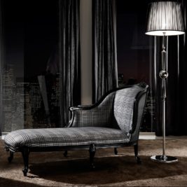 A modern black-and-white Classic Houndstooth Louis High End Designer Chaise Longue with plaid upholstery sits beside a tall floor lamp, in front of large windows overlooking the city skyline at night. Represents a Wednesday inspired interior design style.