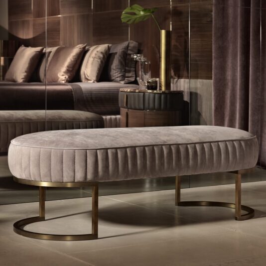 A modern bedroom features the Contemporary Italian Designer Leather Upholstered Bench with vertical tufting and gold legs, set on a polished floor near a mirrored wall and contemporary furnishings.