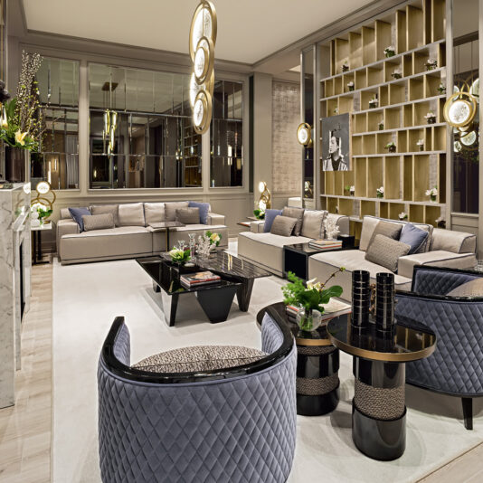 Contemporary Italian Designer Round Side Table A contemporary living room with an elegant, symmetrical design features gray sofas, plush armchairs, a Contemporary Italian Designer Round Side Table, and a black coffee table. A wall adorned with an open shelving unit displaying decor and modern hanging light fixtures with greenery adds a touch of sophistication.