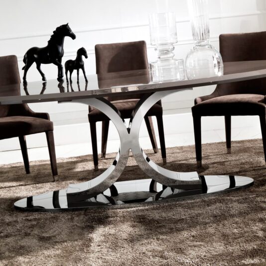 A modern dining room showcases a Contemporary Italian Oval Dining Table with a sleek glass top and an elegant, curved metal base. The table is surrounded by brown upholstered chairs on a plush brown rug, adorned with decorative glassware and two black horse sculptures.
