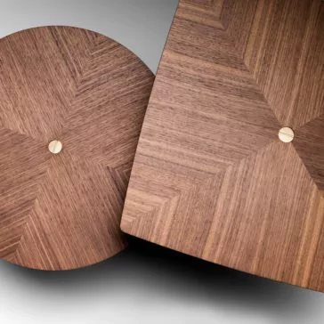 Close-up of two Contemporary Walnut Designer Side Tables showcasing geometric designs on their wooden tabletops. The circular tabletop exhibits a radiating pattern, and the square tabletop mirrors this design. Both tables feature a small, round metal accent at the center and are crafted from rich walnut wood. They are positioned at an angle against a neutral backdrop.