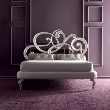 Elegant bedroom with a plush, purple carpeted floor featuring a Designer White Leather Bed adorned with a decorative, swirling headboard. The paneled walls are painted in a matching purple hue, creating a sophisticated and cohesive look.