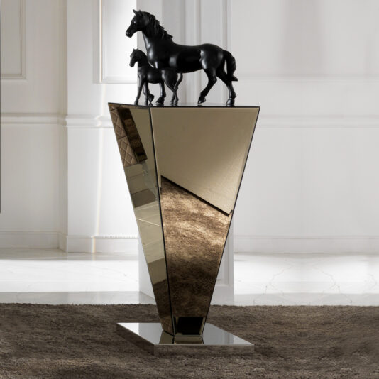 A modern art sculpture featuring two black horse figures, a mare and a foal, standing on top of the Glass Graduated Ornamental Pedestal. The pedestal's sleek, polished surfaces mirror the surroundings, set against a neutral-toned interior.