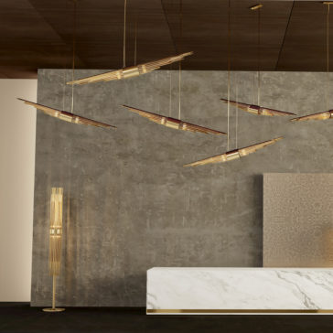 A modern interior features a minimalist design with a marble reception desk and a textured concrete wall. Several sleek, angled pendant lights hang from the dark ceiling, and to the left stands the stunning Gold Plated Designer Modern Floor Lamp, showcasing a harmonious design.