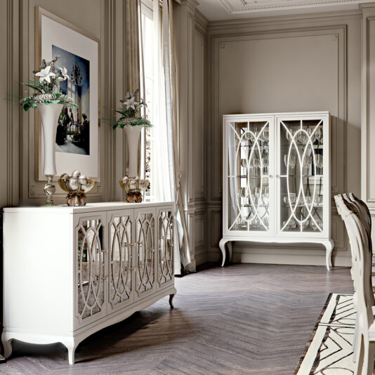 A sophisticated dining room features elegant High End Italian White Fretwork Display Cabinets with mirrored patterns. A buffet table is adorned with decorative vases, and a modern art piece hangs above. The room has large windows with long curtains and hardwood herringbone flooring.
