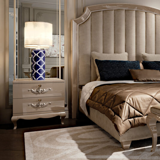 High End Modern Designer Bedside Drawers Luxurious bedroom with tufted headboard, beige bedding, and high-end modern designer bedside drawers. A blue and white patterned lamp adds a touch of elegance. The décor includes ornate mirrors, plush pillows, and rich wood details, creating an opulent and inviting atmosphere.