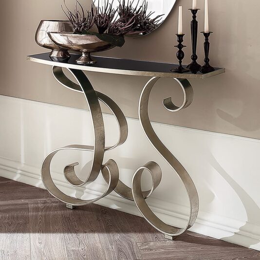 Italian Designer Champagne Silver Leaf Console The Italian Designer Champagne Silver Leaf Console stands against the wall, topped with decorative bowls, branches, and tall candle holders. A herringbone wood floor and a round mirror add to the elegant scene.