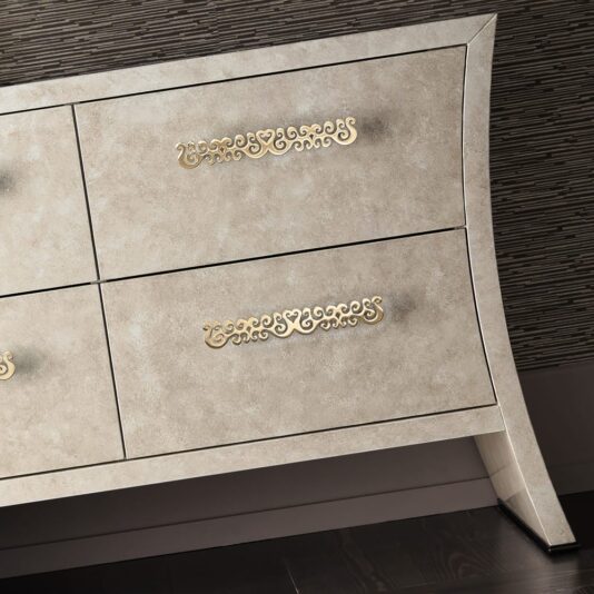 The Italian Designer Seashell Effect Drawers is a light beige, vintage-style dresser featuring four seashell effect drawers with ornate, gold-colored handles. This elegant piece boasts gracefully curved legs and a textured finish, making it a perfect addition against dark, striped wallpaper and on a dark wood floor.