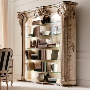 Large Italian Carved Designer Bookcase The Large Italian Carved Designer Bookcase, featuring glass shelves and decorative carvings, showcases books, bowls, and vases against a white wall beside a striped chair.