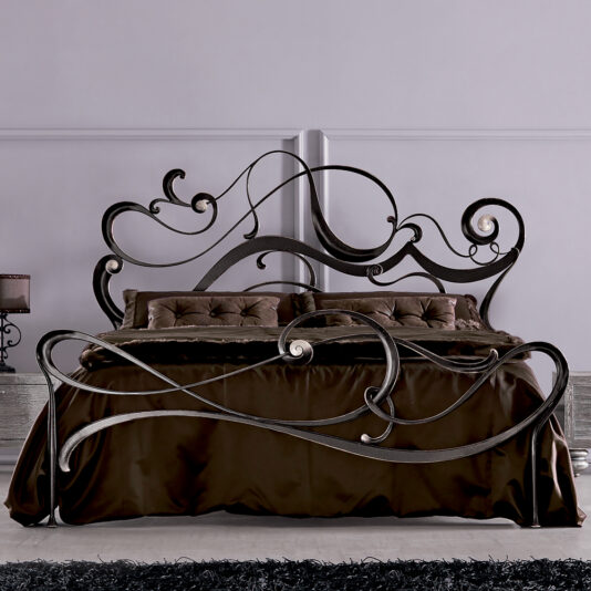 The Luxurious Iron Designer Ornate Twirl Bed showcases swirling metal designs on the headboard and footboard, complemented by a dark brown bedspread and pillows against a light wall.