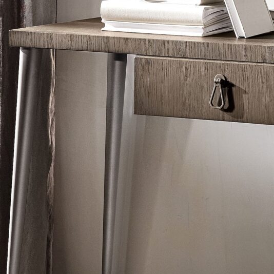 A close-up image of the Luxury Italian Designer Contemporary Desk showcasing a single drawer with a small metal handle. Books are placed on its sleek, modern wooden tabletop, supported by thin, angled legs. A curtain is partially visible to the left of this sophisticated piece.