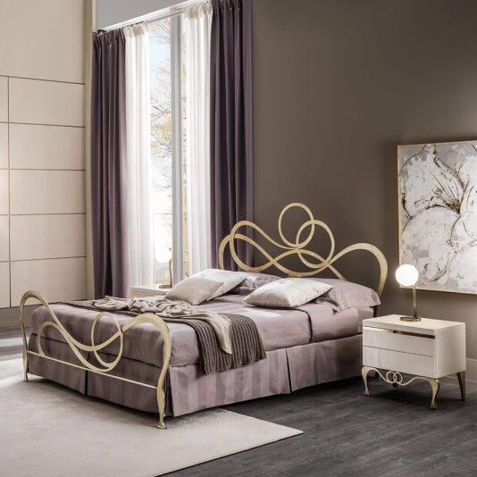 Luxury Mother Of Pearl Bedside Table A modern bedroom showcases a lavish double bed with an ornate metal frame and headboard, adorned in mauve bed linens. Next to it is the Luxury Mother Of Pearl Bedside Table, topped with a round lamp. Tall windows draped in purple fabric and a contemporary abstract painting on the wall complete the elegant setting.