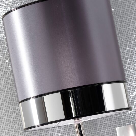 A close-up of the Luxury Platinum Plated Italian Table Lamp, featuring a sleek, cylindrical purple lampshade and a polished chrome base, set against a shiny silver mosaic-patterned tile background. The design creates a contemporary and stylish look.