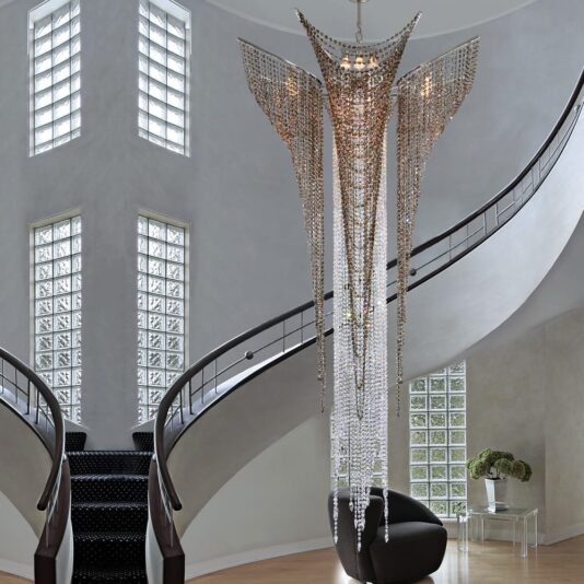 Luxury Stairwell Designer Crystal Pendant Chandelier The Luxury Stairwell Designer Crystal Pendant Chandelier features cascading crystal strands and hangs in a bright entrance hall with curved staircases, glass block windows, and a black chair by a small table topped with flowers.