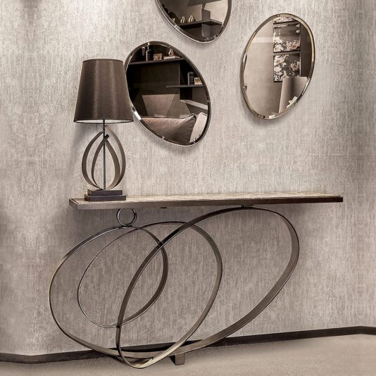 Modern Luxury Marble Ring Console The Modern Luxury Marble Ring Console has overlapping metal ring legs, a brown lamp on top, and sits before three round mirrors on a beige textured wall reflecting a cosy room.