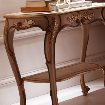 Opulent Carved Italian Bedside Table The Opulent Carved Italian Bedside Table features elegant, intricate carvings and graceful curved legs. Books and a string of pearls are neatly placed on its tabletop, enhancing its antique charm against the backdrop of a simple, white wall.