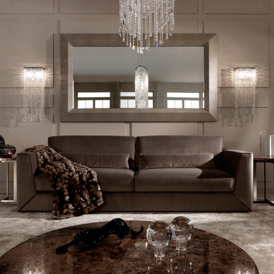 A luxurious living room boasts the Exclusive Modern Italian Chocolate Brown Velvet Sofa with a fur throw, a large mirror, crystal wall sconces, chandelier, and a round marble coffee table topped with decorative glass orbs for elegant style.