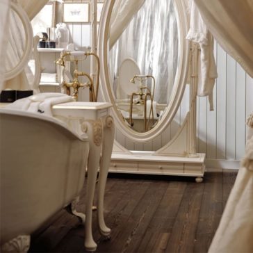 Designer Italian Rococo Console Table with mirror A vintage-style bathroom featuring a free-standing white bathtub with claw feet, a large oval standing mirror, and an elegant vanity table with ornate legs. Brass fixtures adorn the space, complemented by a Designer Italian Rococo Console Table with Mirror. White wooden paneling covers the walls, and the floor is dark hardwood.