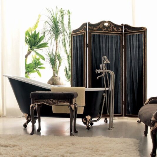 A luxurious bathroom featuring a vintage black clawfoot tub with ornate gold legs, greenery in the background, a small dark wood stool with a towel draped over it, an Exclusive Black and Gold Italian Dressing Screen, and a plush white rug on the floor.