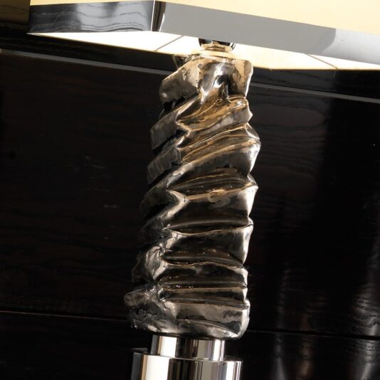 Introducing the Exclusive Platinum Plated Majolica Table Lamp, featuring a brilliant crumpled metal base paired with a sleek rectangular white lampshade. The sculptural, folded design of the base reflects light in diverse directions, making a stunning contrast against its dark, polished surroundings.