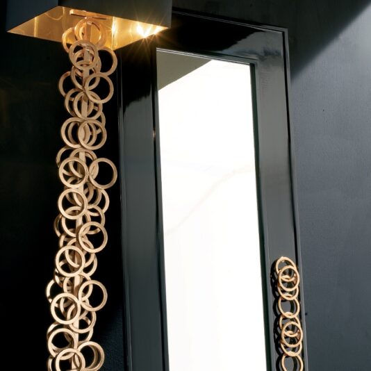 High End Contemporary Italian Black Floor Mirror The High End Contemporary Italian Black Floor Mirror exudes sophistication with its sleek black frame and distinctive design of vertically hanging interlocking golden rings. This exquisite fixture emits light from the top, casting shadows on adjacent surfaces and illuminating the rings in an elegant display similar to that of a high-end floor mirror.