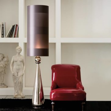 Large Exclusive Italian Majolica Lamp An elegant interior space featuring a modern tall floor lamp with a cylindrical shade next to a glossy red chair. A classical statue and the Large Exclusive Italian Majolica Lamp sit on a white shelf in the background, which also holds books, against a white wall with a grid-like design.