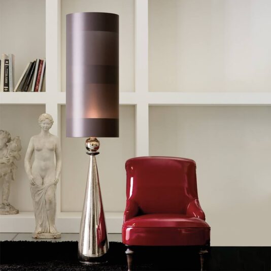 An elegant interior space featuring a modern tall floor lamp with a cylindrical shade next to a glossy red chair. A classical statue and the Large Exclusive Italian Majolica Lamp sit on a white shelf in the background, which also holds books, against a white wall with a grid-like design.