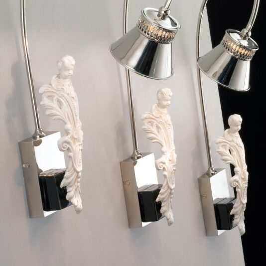 Luxury Majolica Modern Italian Wall Light The Luxury Majolica Modern Italian Wall Light showcases three elegantly wall-mounted lights adorned with intricate off-white carvings of classical cherubs, reminiscent of sophisticated Majolica craftsmanship. Each cherub supports a sleek chrome lamp with a black base. Flexible silver necks and a light-colored wall enhance the fusion of vintage elegance and contemporary design.