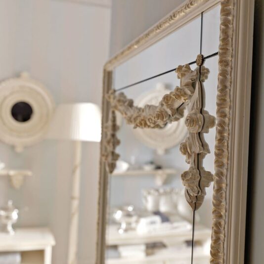 Opulent Italian Bathroom Console with Mirror Close-up of an ornate, rectangular wall mirror with elaborate floral decorations on its frame. In the blurred background, the Opulent Italian Bathroom Console with Mirror is visible, featuring a white lamp and shelves adorned with decorative items, all contributing to a cozy and elegant atmosphere.