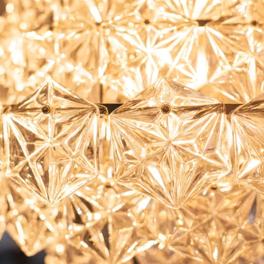 Large Faceted Glass Pendant Chandelier Close-up of the Large Faceted Glass Pendant Chandelier, featuring intricately cut star-shaped crystals that reflect and refract warm golden light, creating a sparkling and luxurious effect.